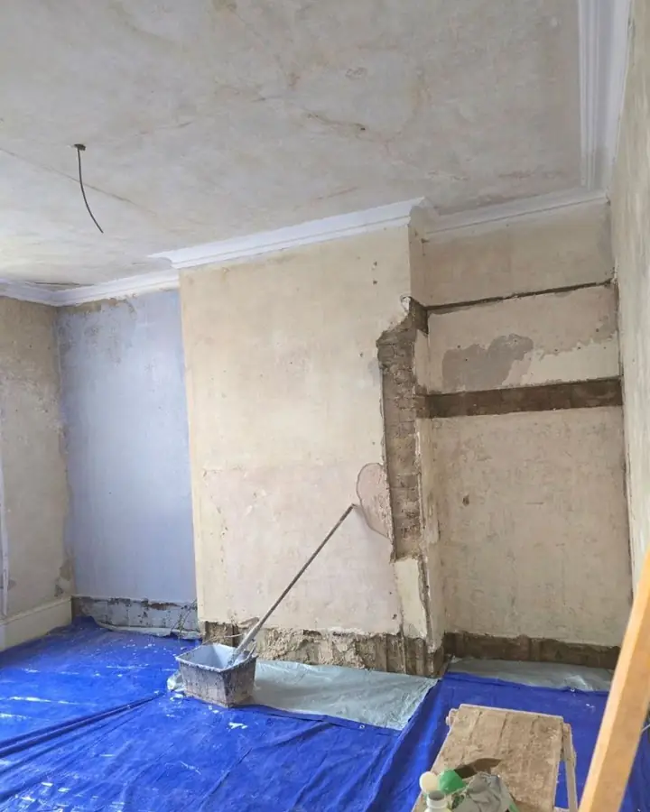 Room with a chimney breast stripped back to bare plaster and brick, floor sheeted in blue