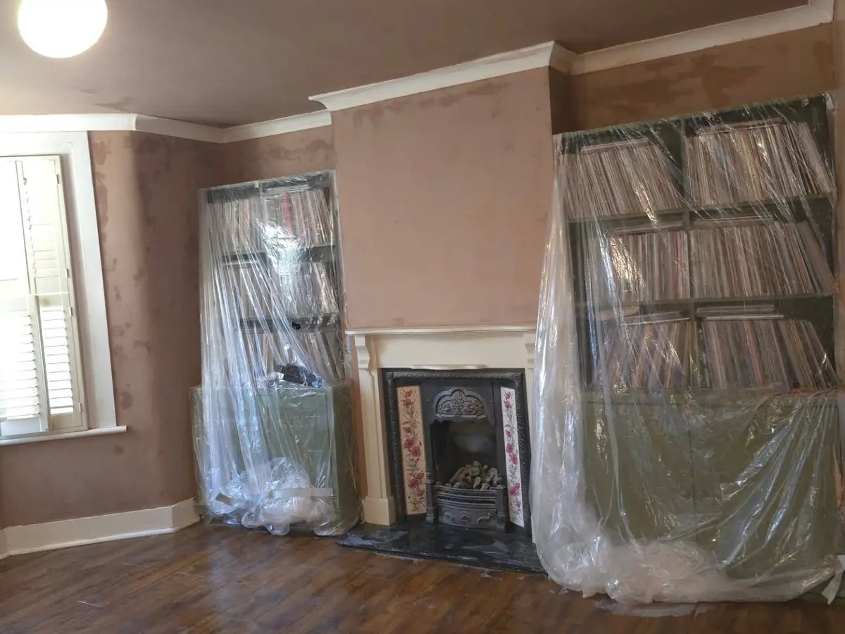 Bookshelves wrapped in plastic sheeting while the walls around them are freshly plastered