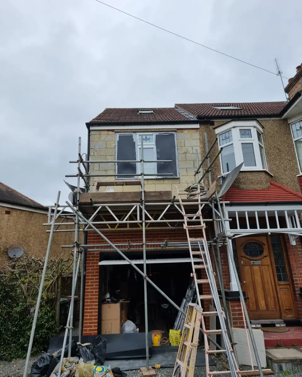 Semi-detached house front in bare blockwork under scaffolding, before pebbledash